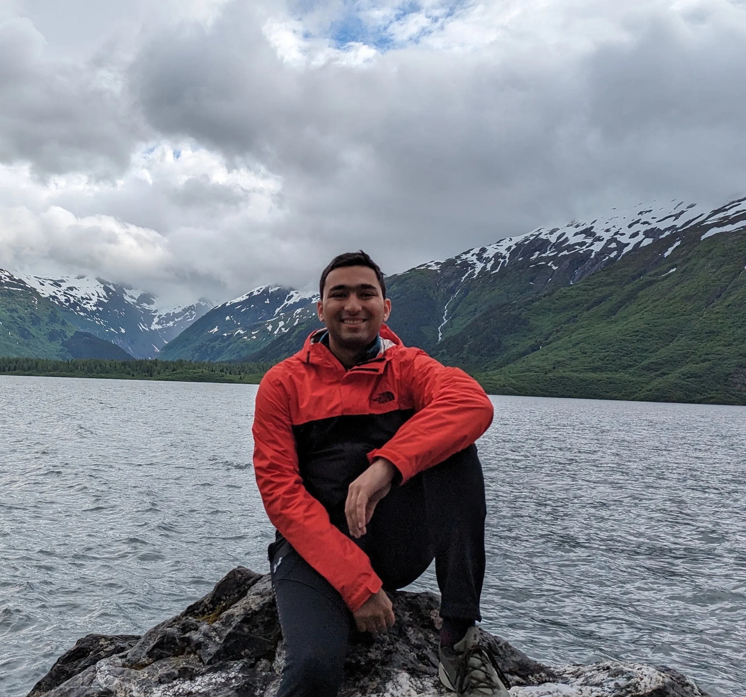 Man sitting on a rock in a red raincoat in front of a lake